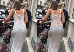 Woman pushing bike on street wearing thin white dress that is showing blue panties and white bra.